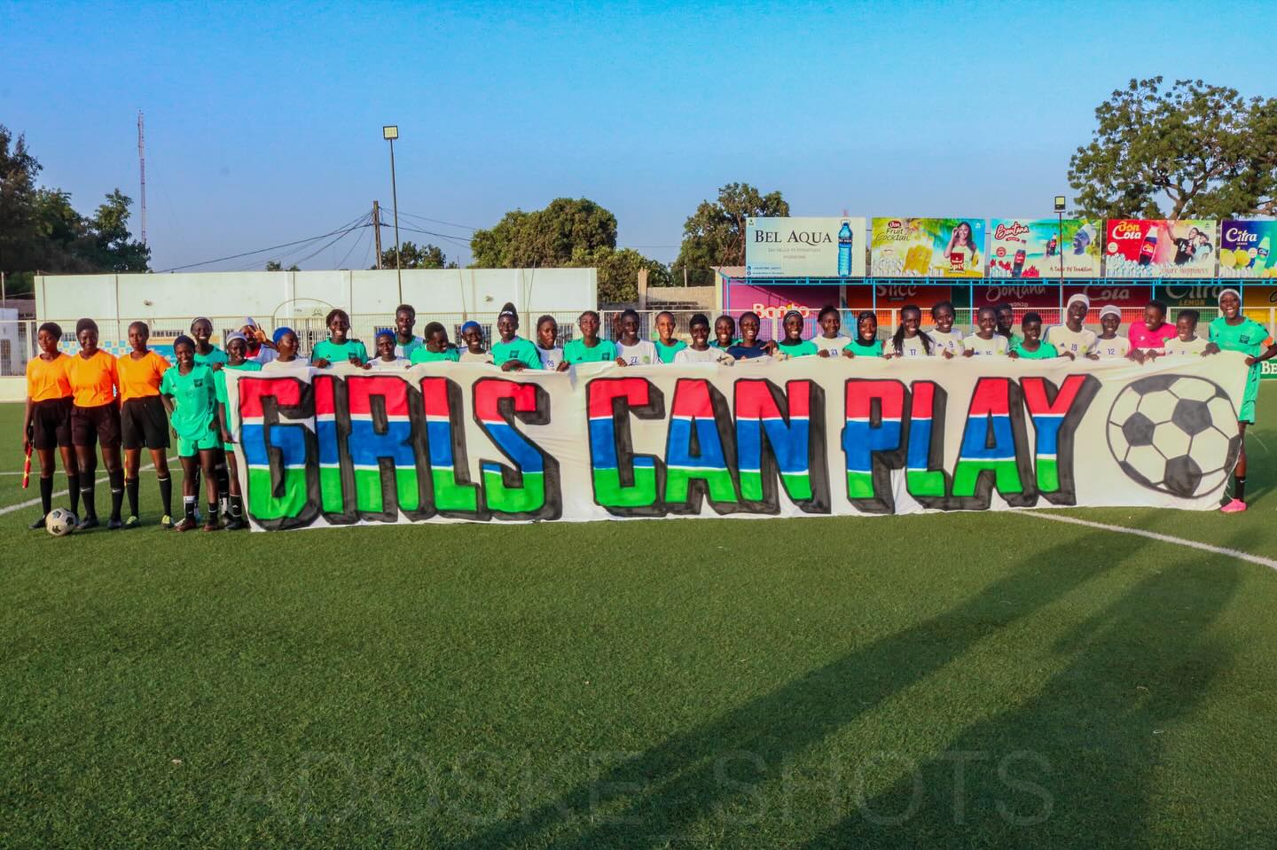 Spielerinnen auf dem Fußballplatz hinter einem großen „Girls Can Play“-Banner